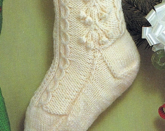 May include: A white knitted Christmas stocking with a cable knit pattern and a leafy design. The stocking is hanging on a green wall with a white bow and a candy cane.