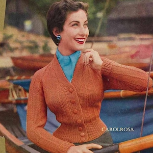May include: A vintage photo of a woman wearing a fitted, orange cardigan with a V-neck and button closure. She is wearing a blue scarf and has her hair styled in a short, neat bob.