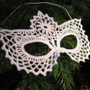 Könnte beinhalten: Weiße Häkelmaske mit einem zarten Blumenmuster. Die Maske hat eine traditionelle Augenform und ist mit einer kleinen Blume oben verziert.