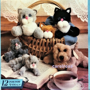 May include: A set of 12 pom pom animal patterns, featuring a grey cat with glasses, a black cat, a brown and white cat, a grey cat, and a brown dog. The animals are sitting in a wicker basket and on a book. The text "12 POM POM ANIMALS" is visible in the image.