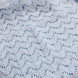 May include: White crocheted shawl with a delicate lace pattern. The shawl is made with a fine yarn and has a soft, airy feel.