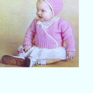 May include: A pink knitted baby sweater with a white trim and a matching pink knitted hat with a white trim. The sweater has a wrap-around style with a button closure.