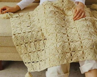 May include: A crocheted throw blanket in a cream colour with a square pattern. The blanket is draped over a sofa and has tassels on the ends.