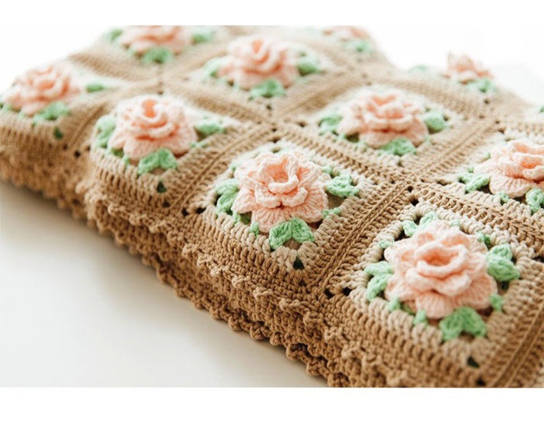 May include: A crocheted blanket with a brown and white pattern and pink and green flowers.