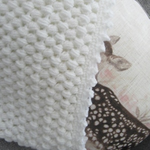 May include: A white crocheted baby blanket with a textured, puffy stitch pattern.