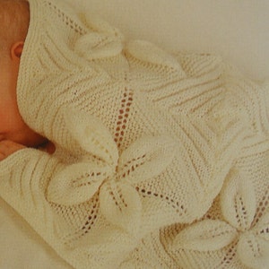 May include: A white knitted baby blanket with a delicate floral pattern. The blanket is made of soft yarn and is perfect for keeping a baby warm and cozy.