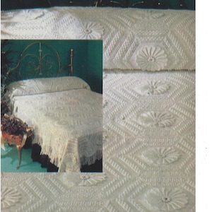 Puede incluir: Una colcha blanca de ganchillo con un patrón floral y flecos. La colcha está sobre una cama con una cabecera de metal negro.
