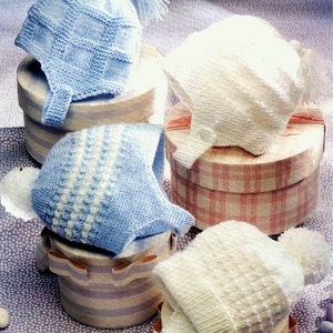 May include: Four knitted baby hats in blue and white colors. The hats are displayed on top of round boxes with patterned designs. The hats are made with 4 ply yarn and double knitting techniques.