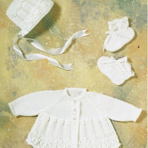 May include: A white knitted baby set consisting of a long-sleeved cardigan with three small buttons, a bonnet with a white satin ribbon tie, and a pair of matching booties. Each piece features a delicate, intricate openwork pattern.