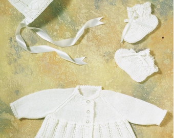 May include: A white knitted baby set consisting of a long-sleeved cardigan with three small buttons, a bonnet with a white satin ribbon tie, and a pair of matching booties. Each piece features a delicate, intricate openwork pattern.