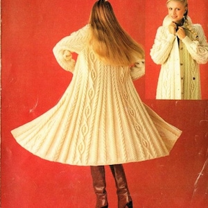 May include: A long, white knitted cardigan with a cable knit pattern. The cardigan is shown on a model wearing brown boots.