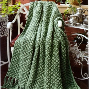May include: A green crocheted throw blanket with a textured pattern, draped over a white chair. The blanket has a fringe border.