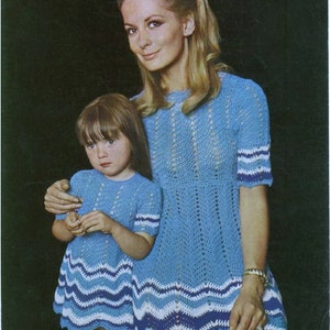 May include: A mother and daughter wearing matching blue crochet dresses with white and blue trim. The dresses have a loose fit and short sleeves. The mother's dress has a more open crochet pattern than the daughter's dress.