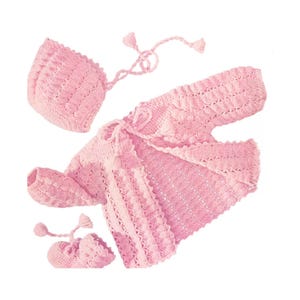 Puede incluir: Un conjunto de bebé de ganchillo rosa claro que incluye un gorro, una chaqueta y patucos. El conjunto presenta un patrón texturizado y detalles de borlas. La chaqueta tiene un cierre de lazo. Los patucos tienen forma redondeada.