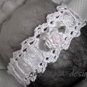 Puede incluir: Una diadema blanca de ganchillo con una flor de satén y un delicado diseño de encaje. La diadema es perfecta para una recién nacida.