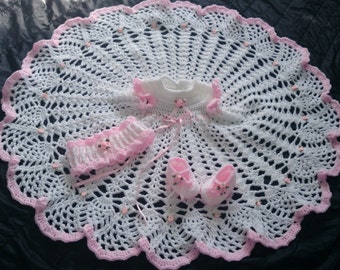 Könnte beinhalten: Ein weiß-rosa gehäkeltes Baby-Set, bestehend aus einem Kleid, einem Stirnband und Babyschuhen. Das Set hat einen gewellten Rand und ist mit kleinen rosa Blumen und Bändern verziert. Der Durchmesser der Decke beträgt ca. 76 cm.