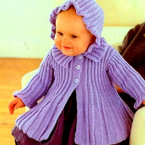 May include: A purple knitted baby cardigan with a hood and buttons. The cardigan has a scalloped edge around the hood and a ruffled collar.