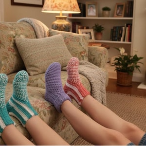 Könnte beinhalten: Gehäkelte Socken in Türkis, Lila und Koralle mit weißen Streifen werden gezeigt. Die Socken werden mit einem floral gemusterten Sofa im Hintergrund präsentiert. Die Socken sind handgefertigt und scheinen bequem und warm zu sein.