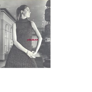 May include: A black and white photo of a woman wearing a sleeveless, turtleneck dress with a ribbed texture. The dress has a fitted bodice and a flowing skirt. The woman is standing in a hallway with a potted plant in the background.