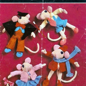May include: Four knitted mouse toys with different outfits. The mice are wearing a graduation cap and gown, a pink shirt and blue overalls, a pink sweater and blue skirt, and a red sweater and blue scarf. The toys are on a pink background. The pattern is from Copley Cadette 2403.