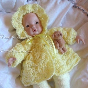 May include: A yellow crocheted baby doll outfit with a matching bonnet and a small teddy bear. The doll has a porcelain face with painted features.