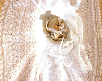 May include: Two white crocheted baby blankets with delicate lace edging. One blanket features a diamond pattern, while the other has a more open weave. The blankets are arranged on a wooden surface with a small bowl of seashells in the centre.