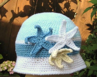 May include: A crocheted hat with a blue, white, and light blue color scheme. The hat is decorated with three crocheted starfish in different colors.