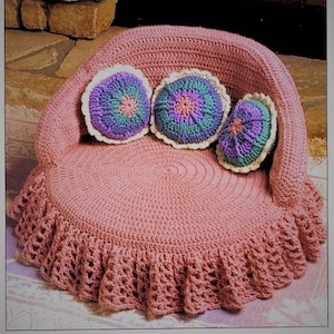 May include: A crocheted pink armchair with a ruffled skirt and three colorful crocheted pillows. The pillows have a circular design with shades of purple, green, and white.