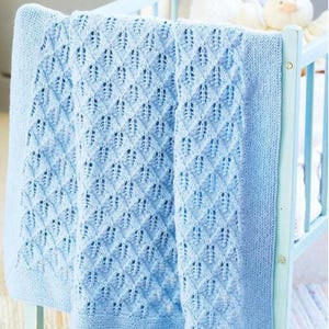Könnte beinhalten: Eine hellblaue gestrickte Babydecke mit einem detaillierten Lochmuster, drapiert über einem hellblauen Kinderbett. Die Decke hat ein strukturiertes Design und einen durchgehenden Rand. Ein weißes Stofftier ist im Hintergrund zu sehen.