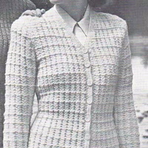 May include: A woman wearing a white knitted cardigan with a button-up front and a white collared shirt underneath. The cardigan has a textured pattern and is worn over a skirt.