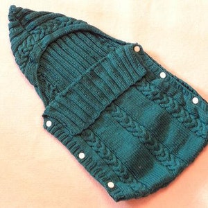 Puede incluir: Un saco de dormir para bebé de punto azul turquesa con botones blancos.