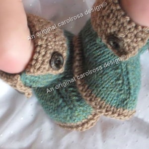 Puede incluir: Un par de botitas de bebé de punto color verde azulado y marrón con un botón en cada botita. Las botitas tienen un puño de punto marrón y están hechas con un punto de tejido texturizado. El texto "An original carolrosa design®" es visible en las botitas.