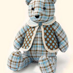 Pu&ograve; includere: Un orsacchiotto di peluche blu e marrone a quadri con un gilet marrone con pois blu e un bordo in pizzo bianco. L'orso &egrave; seduto con le gambe incrociate.