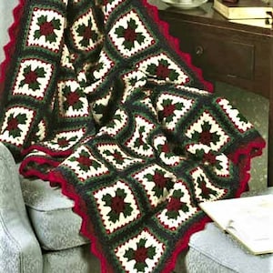 May include: A crocheted throw blanket with a red, green, and white pattern. The blanket is made of squares with a leaf design in the center. The blanket is draped over a chair.