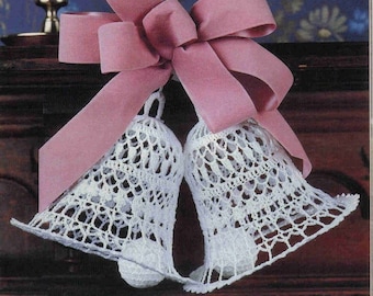 May include: Two white crocheted bells with a pink satin bow. The bells are tied together with the bow and are hanging from a wooden surface.