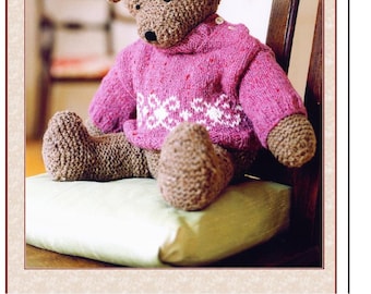 May include: A brown knitted teddy bear wearing a pink knitted sweater with a white snowflake pattern sits on a green cushion. The teddy bear is sitting on a wooden chair. The text "Need A Hug Real Bad Teddy!" is at the top of the image.