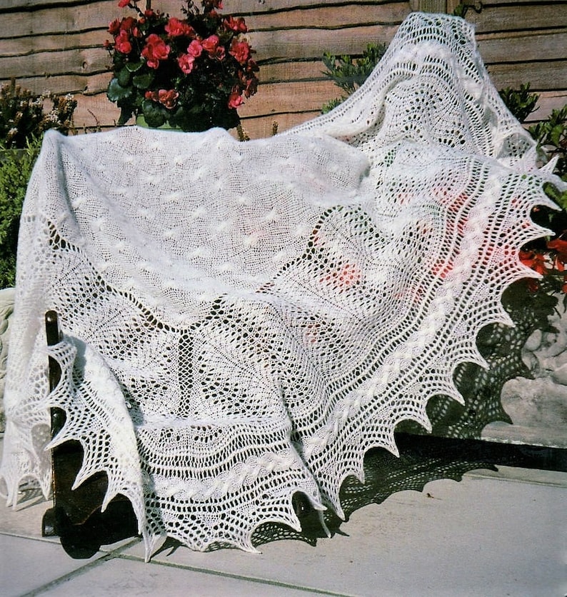 May include: A white crocheted shawl with a delicate lace pattern. The shawl is draped over a wooden bench and has a scalloped edge.