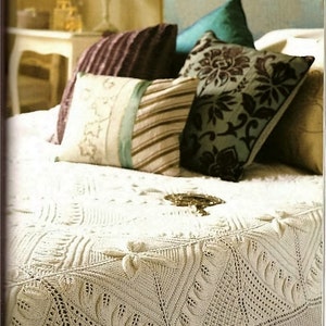 May include: A white crocheted bedspread with a detailed pattern and fringe trim. The bedspread is on a bed with pillows in various colors and patterns, including teal, brown, and purple.