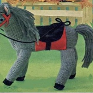 Pode incluir: Um cavalo de brinquedo de malha cinza com uma sela vermelha e preta. O cavalo tem uma rédea preta e uma cauda longa cinza.