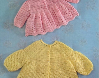 May include: Two crocheted baby sweaters, one pink and one yellow, with button closures. Both sweaters have a scalloped hem and a delicate stitch pattern.