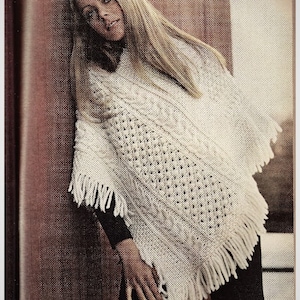 Peut inclure: Un poncho en tricot crème avec des franges. Le poncho présente un motif texturé avec des détails en tricot torsadé et ajouré. Le vêtement est porté sur un haut noir et est présenté sur un fond neutre.