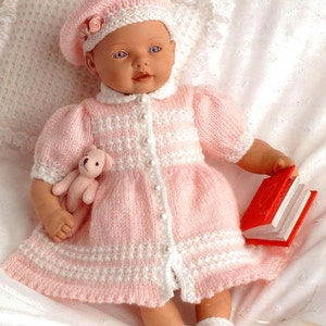 May include: A pink knitted baby doll dress with white trim and pearl buttons. The dress has a matching pink knitted beret with white trim and a pink flower.