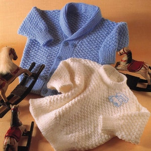 May include: Two knitted baby sweaters, one blue with a shawl collar and buttons, and one white with a small blue car applique.