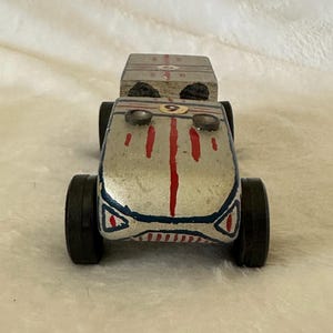 May include: A silver and blue wooden toy race car with red stripes and a number 9 on the hood. The car has black wheels and a wooden box on the back.