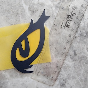 Peut inclure: Un motif noir stylisé sur fond jaune, avec une règle transparente pour la mesure. Le motif a une forme unique avec un sommet pointu et des lignes courbes. La règle affiche des mesures en pouces.