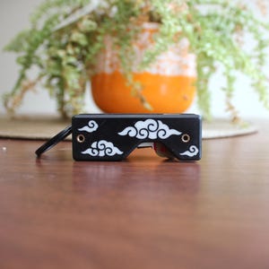 May include: A black and white key holder with a cloud design. The key holder has a rectangular shape with rounded edges and a small metal ring attached. The cloud design is white and covers the surface of the key holder.