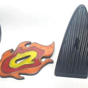 May include: A wooden flame-shaped decoration with orange, red, and yellow layers. Next to it is a black, ridged, triangular object. The items are on a white surface.