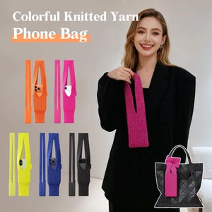 May include: Colorful knitted yarn phone bags in various colors, including orange, pink, yellow, blue, and black. The bags are designed to hold a phone and have a strap. The image also shows a woman wearing a black blazer and holding a pink phone bag.