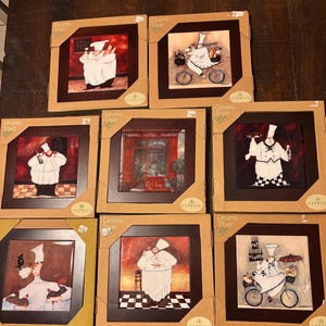May include: A collection of ceramic trivets featuring chef illustrations in various poses. Each trivet is square, framed in dark wood, and packaged in a cardboard box. The chef designs include a chef on a bicycle and a chef holding food.