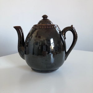 May include: A dark brown ceramic teapot with a rounded body and a lid. The teapot has a shiny glaze and a slightly textured surface.